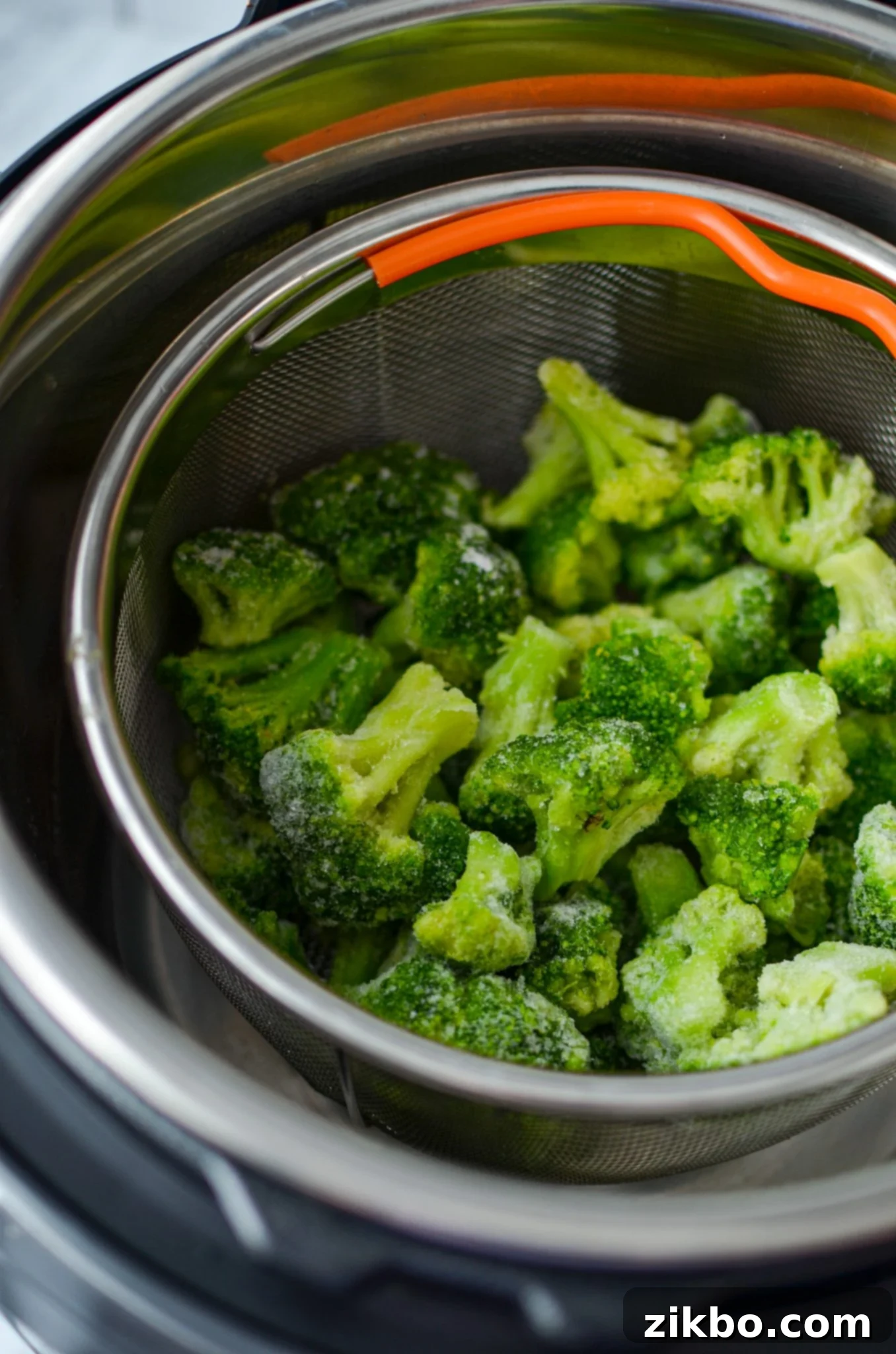 Frozen broccoli resting inside the insert of a steamer basket inside of an Instant Pot.