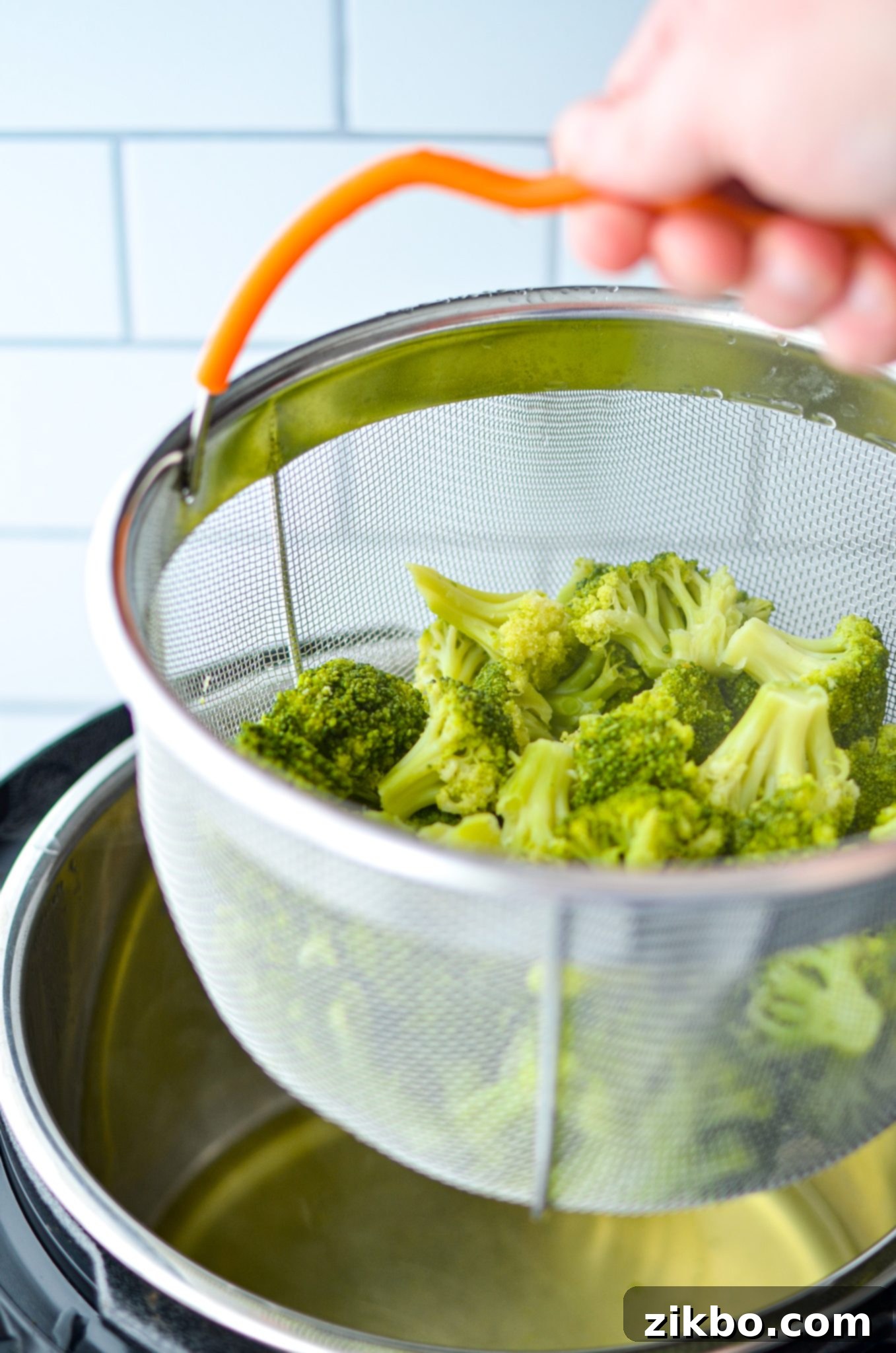 Lifting the steamer basket out of the Instant Pot with cooked broccoli inside.