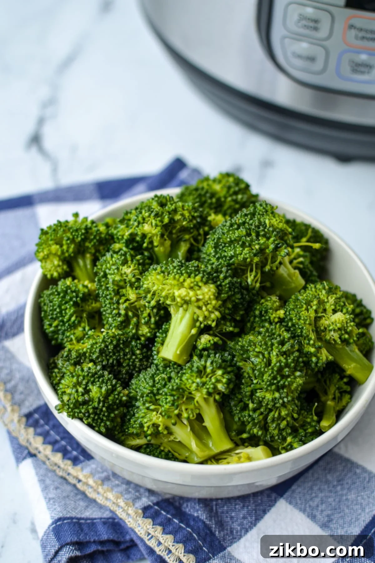 A bowl of cooked broccoli with an Instant Pot in the background, ready to serve.