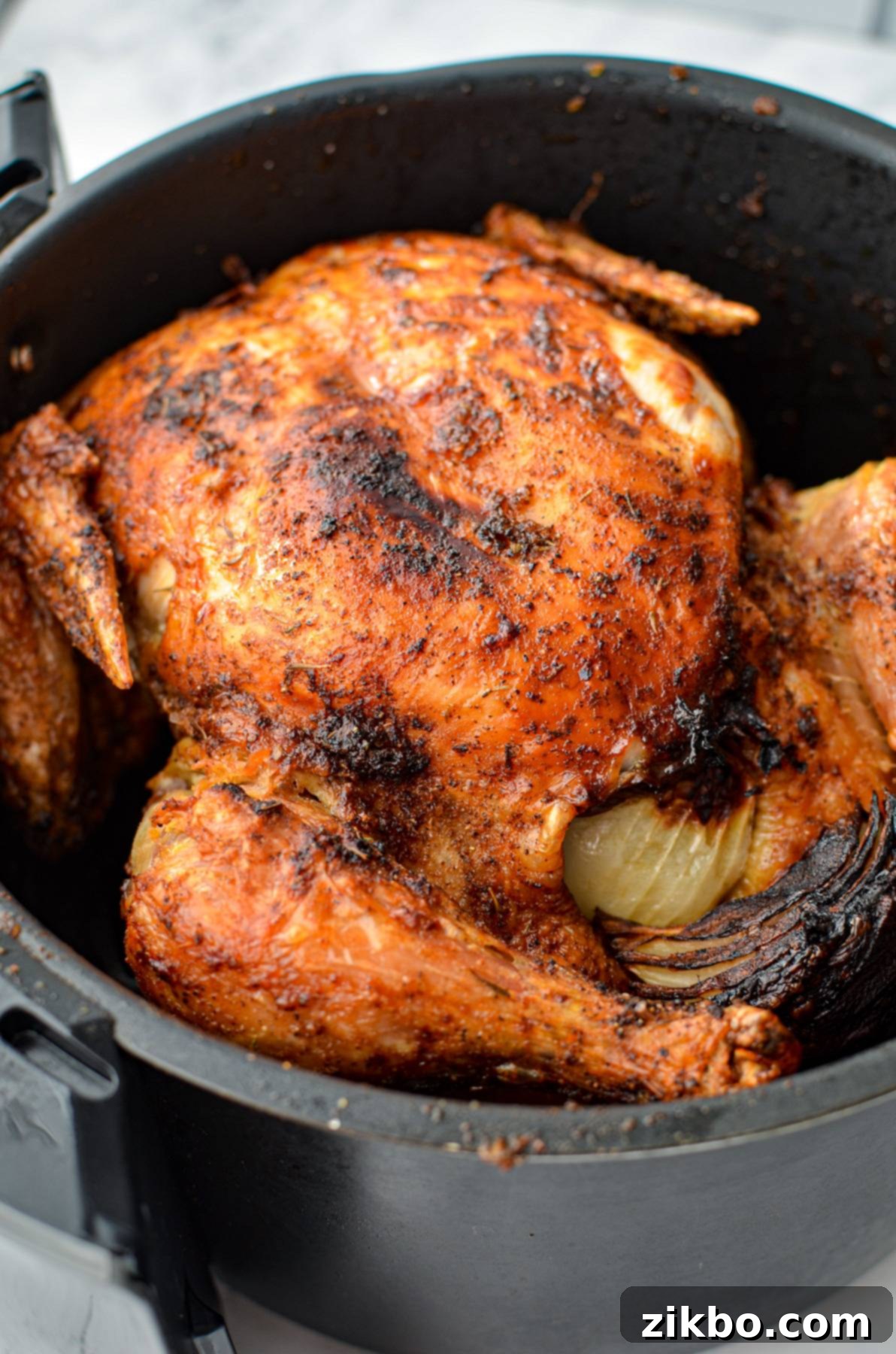 A fully cooked, golden-brown rotisserie-style whole chicken inside an air fryer basket, ready to rest.