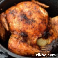 A whole chicken, cooked to perfection in an air fryer basket with golden crispy skin, ready to be served.