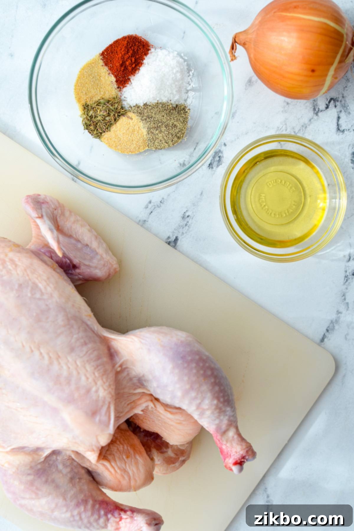 The ingredients needed to make an air fryer whole chicken: chicken, avocado oil, onion, and a blend of seasonings including paprika, garlic powder, onion powder, black pepper, kosher salt, and thyme.