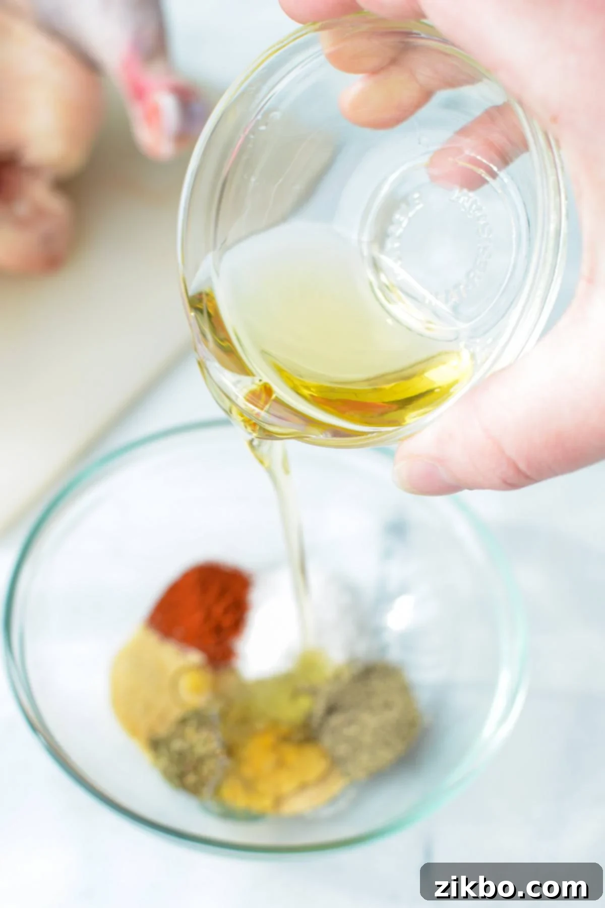 Drizzling avocado oil into a small bowl of mixed dry seasonings.