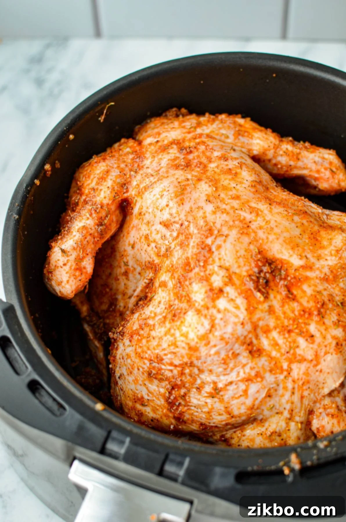 A whole chicken resting breast-side down in an air fryer basket, ready for cooking.