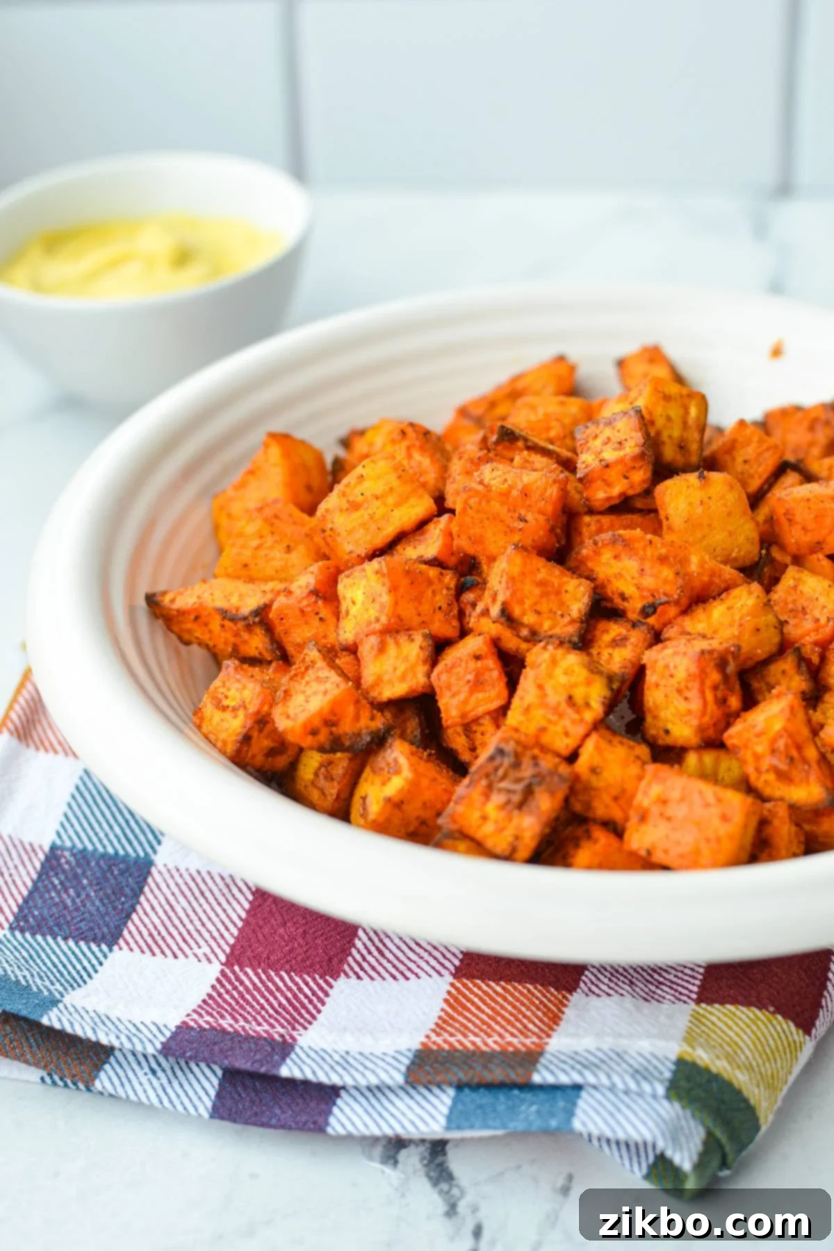 Crispy Air Fryer Sweet Potato Cubes 8 A beautifully arranged bowl of air fryer roasted sweet potato cubes, with a small dish of creamy dipping sauce blurred in the background, ready for a healthy meal.