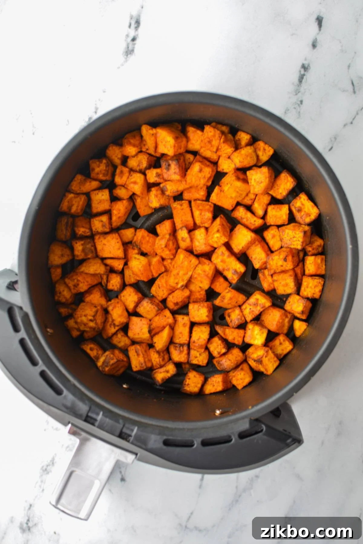 Crispy Air Fryer Sweet Potato Cubes 9 A close-up shot of an air fryer basket filled with perfectly roasted and golden-brown sweet potato chunks.