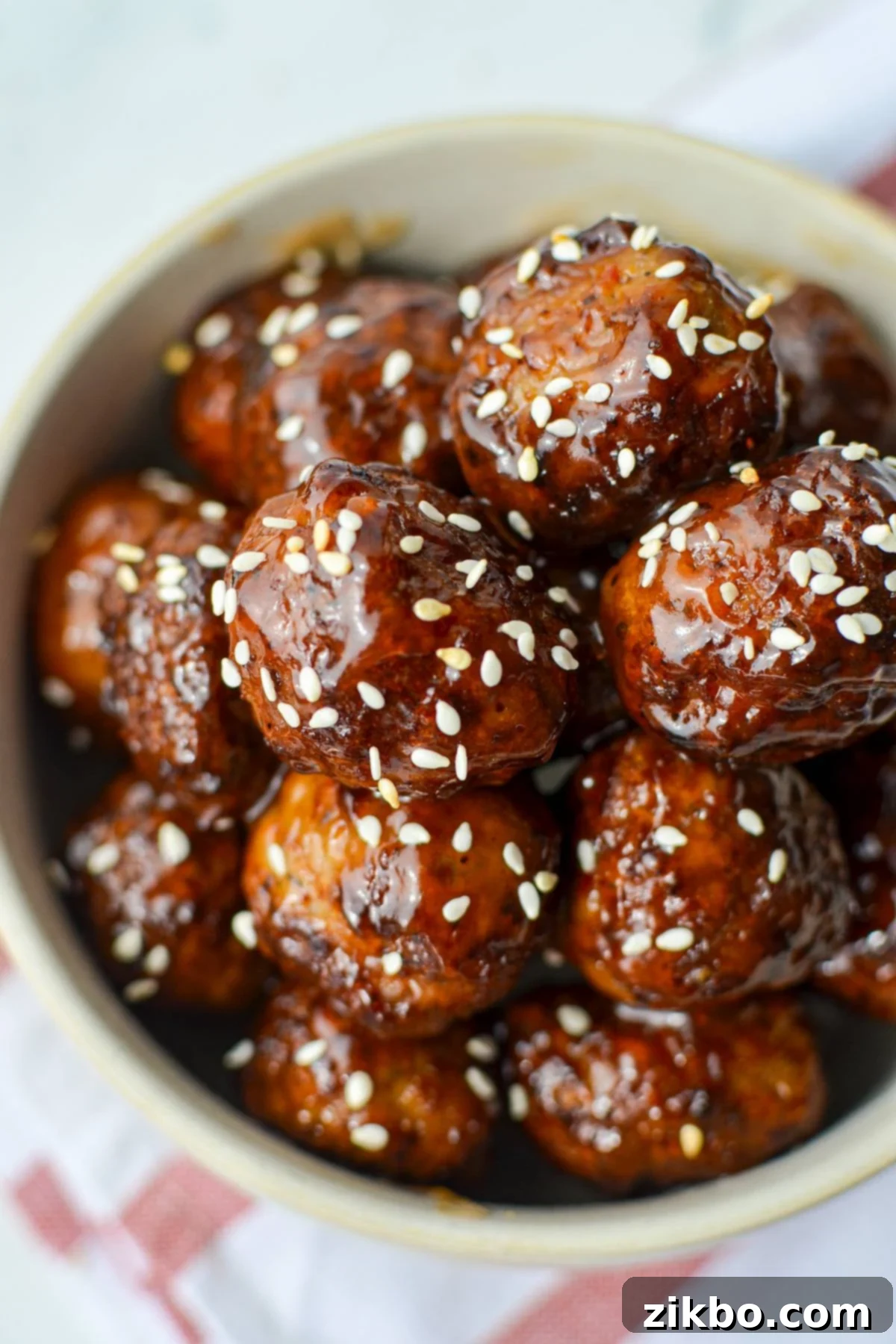 A bowl of glazed meatballs, garnished with sesame seeds, ready to be served.