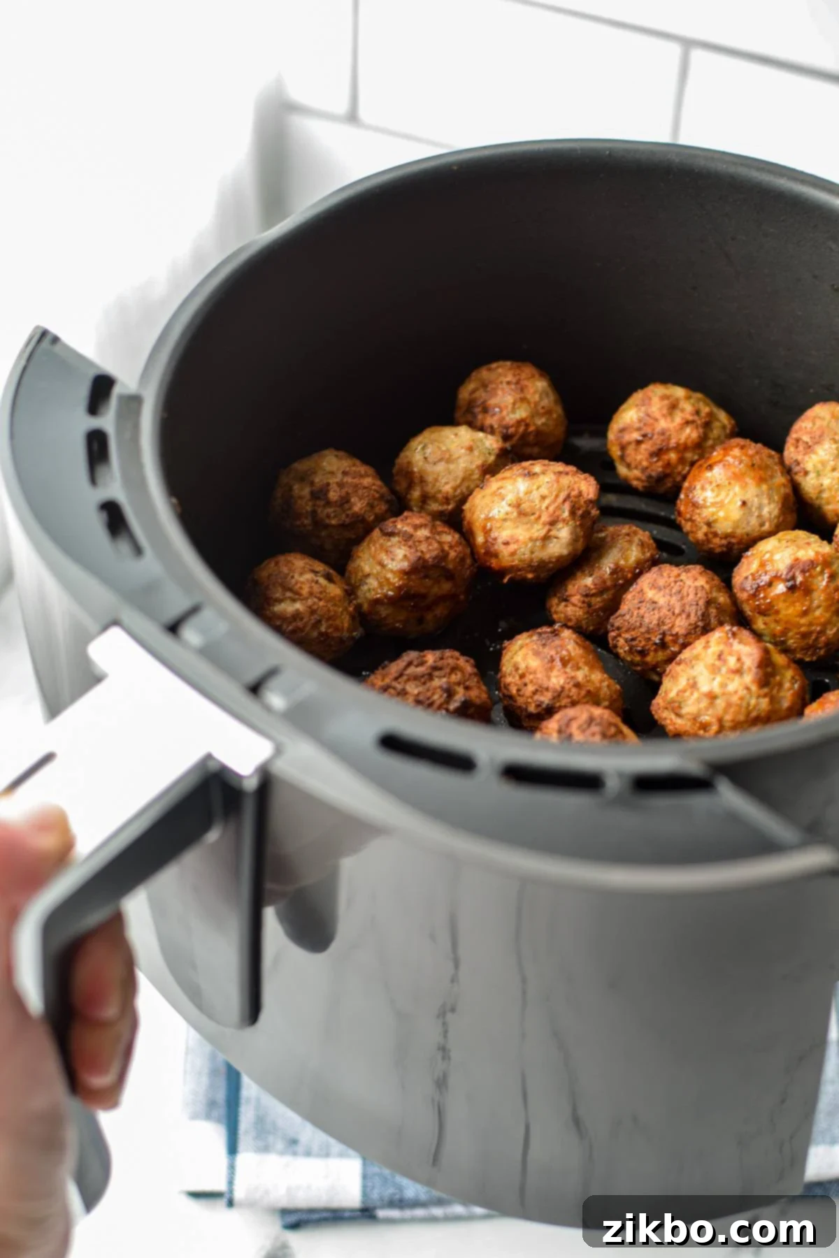 Shaking an air fryer basket full of meatballs to ensure even cooking and browning.