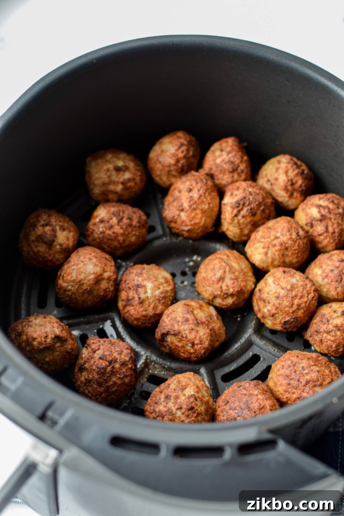 An air fryer basket filled with cooked and browned meatballs.