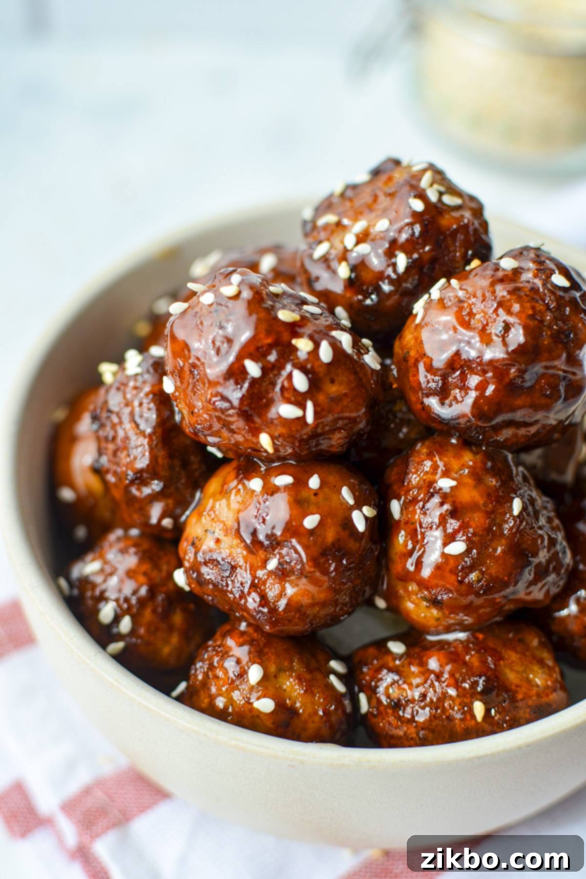 A bowl of glossy glazed meatballs, beautifully garnished with sesame seeds, ready to be enjoyed.