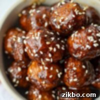 A stack of beautifully glazed meatballs, garnished with fresh sesame seeds, ready to be served.