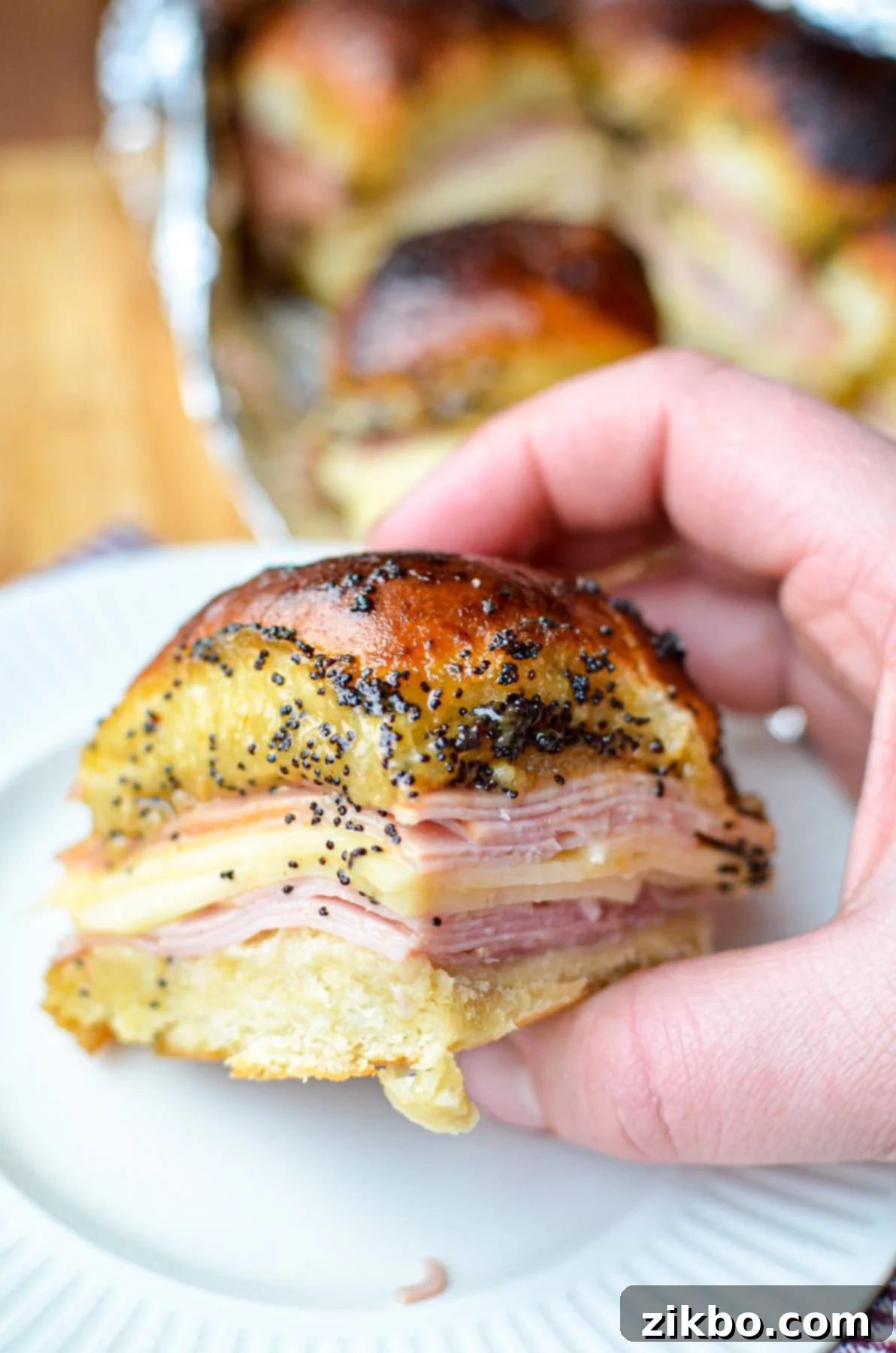 Golden Air Fryer Ham and Cheese Sliders 2 Holding a golden brown ham and cheese slider, covered with a savory poppy seed sauce.