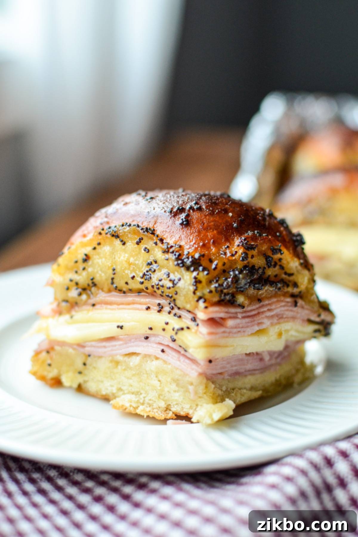 Golden Air Fryer Ham and Cheese Sliders 7 A single air fryer ham and cheese slider on a white plate, showcasing the melted cheese and poppy seed topping.