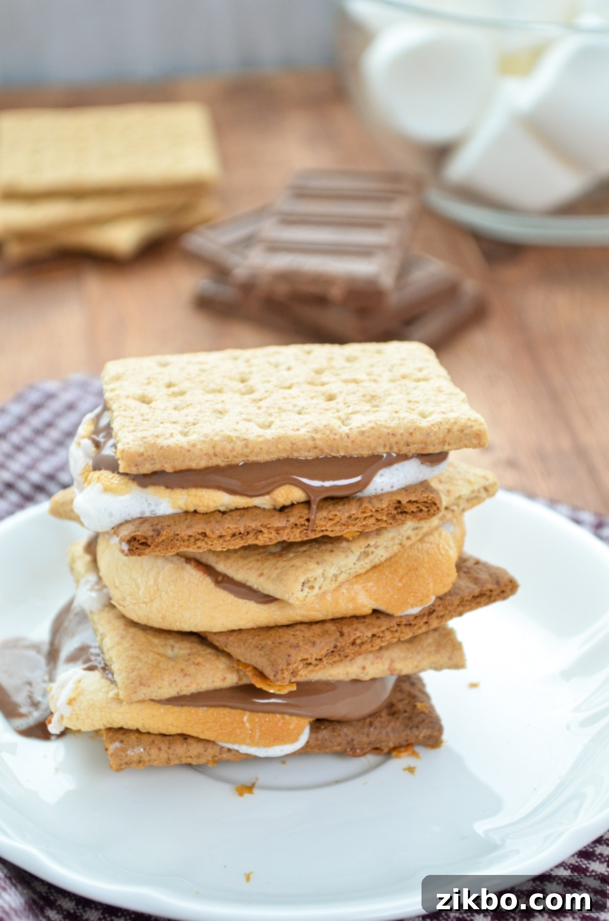 A stack of three s'mores with chocolate, marshmallows, and graham crackers in the background.