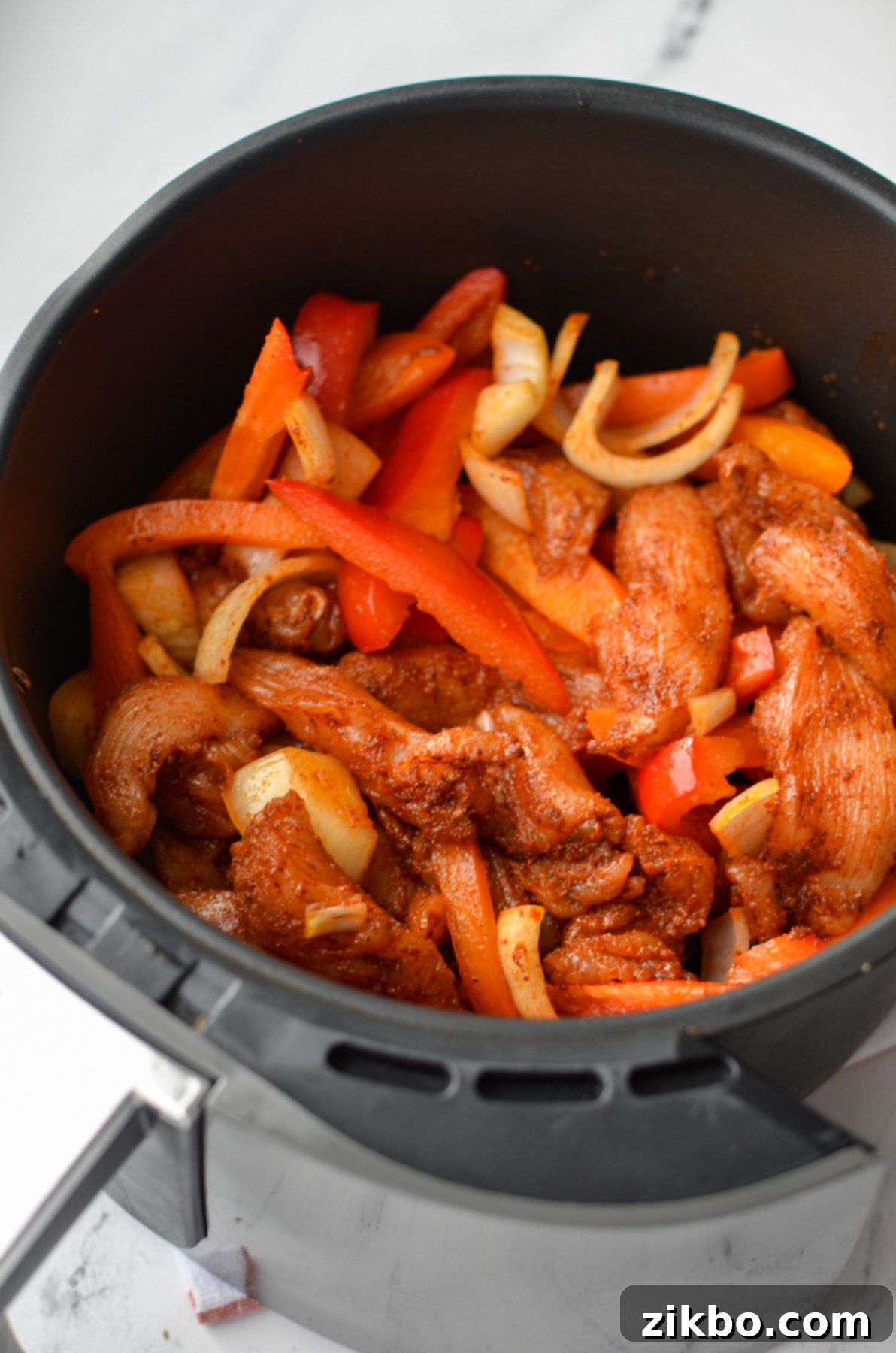 Crispy Air Fryer Chicken Fajitas 6 An air fryer basket filled with uncooked chicken strips, sliced bell peppers, and onions, seasoned and ready for cooking.
