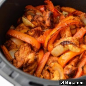 Crispy Air Fryer Chicken Fajitas 10 An air fryer basket with chicken, peppers, and onions inside, beautifully cooked.