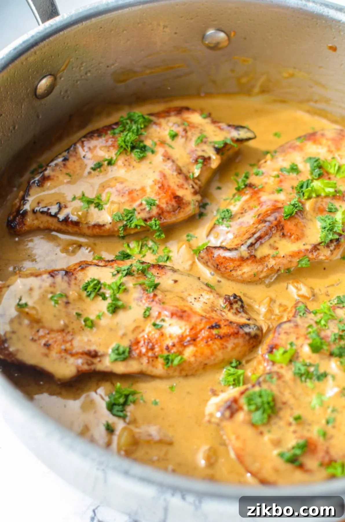 A skillet with chicken breasts and garlic sauce, sprinkled with parsley. A cast iron skillet filled with golden-brown chicken breasts smothered in a rich, creamy garlic sauce, adorned with fresh green parsley.