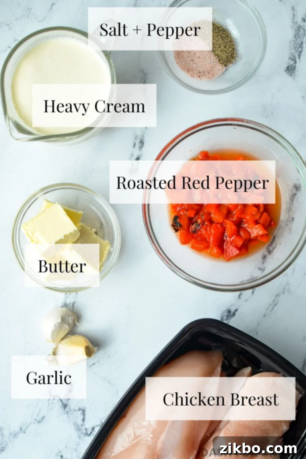 A flat lay of the essential ingredients needed to make creamy roasted red pepper chicken, including chicken breasts, jarred roasted red peppers, butter, garlic, and heavy cream.