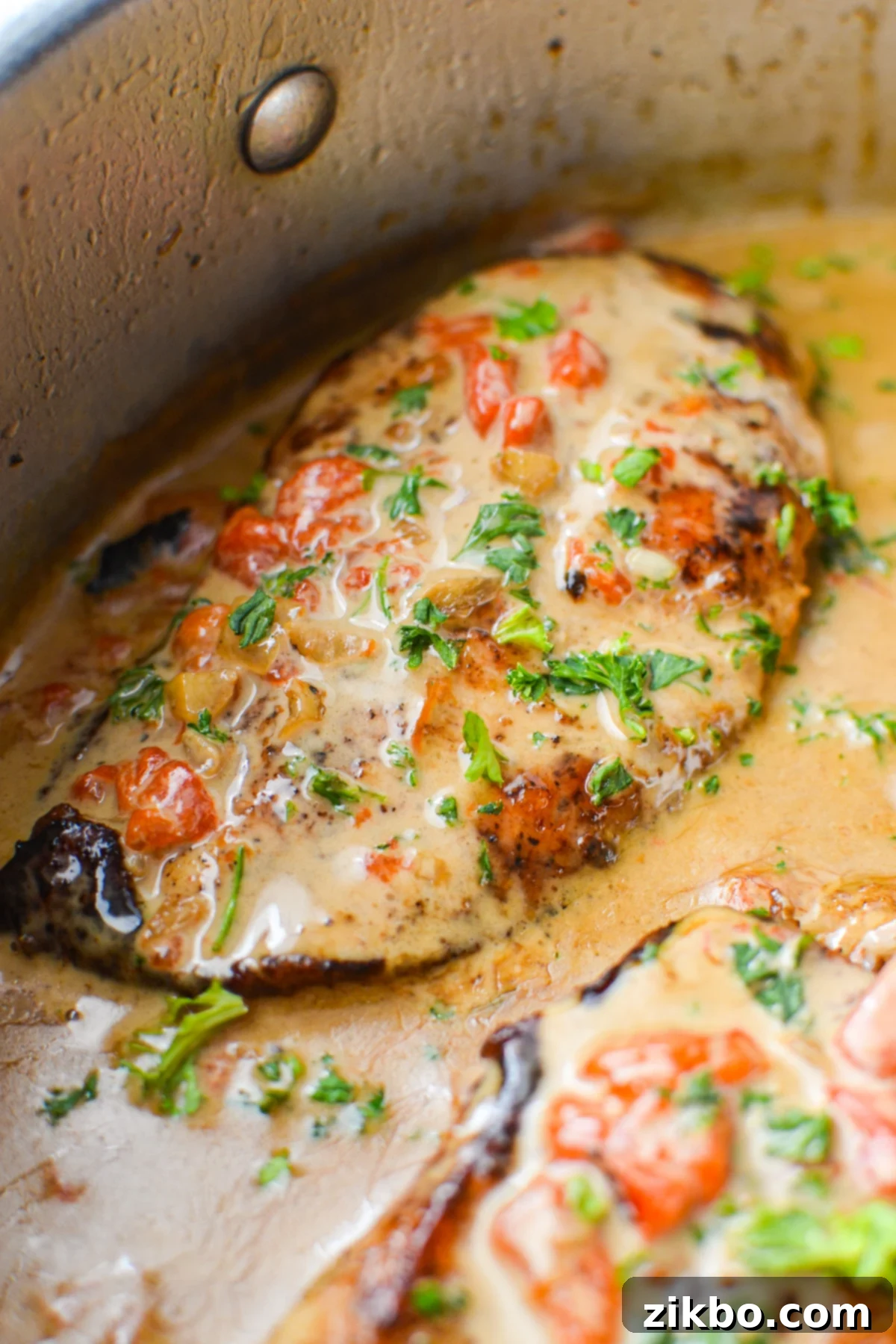 A close-up shot of a perfectly cooked chicken breast smothered in creamy red pepper sauce and garnished with fresh parsley.