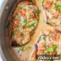 A skillet filled with chicken breasts coated in a red pepper cream sauce, and garnished with parsley.