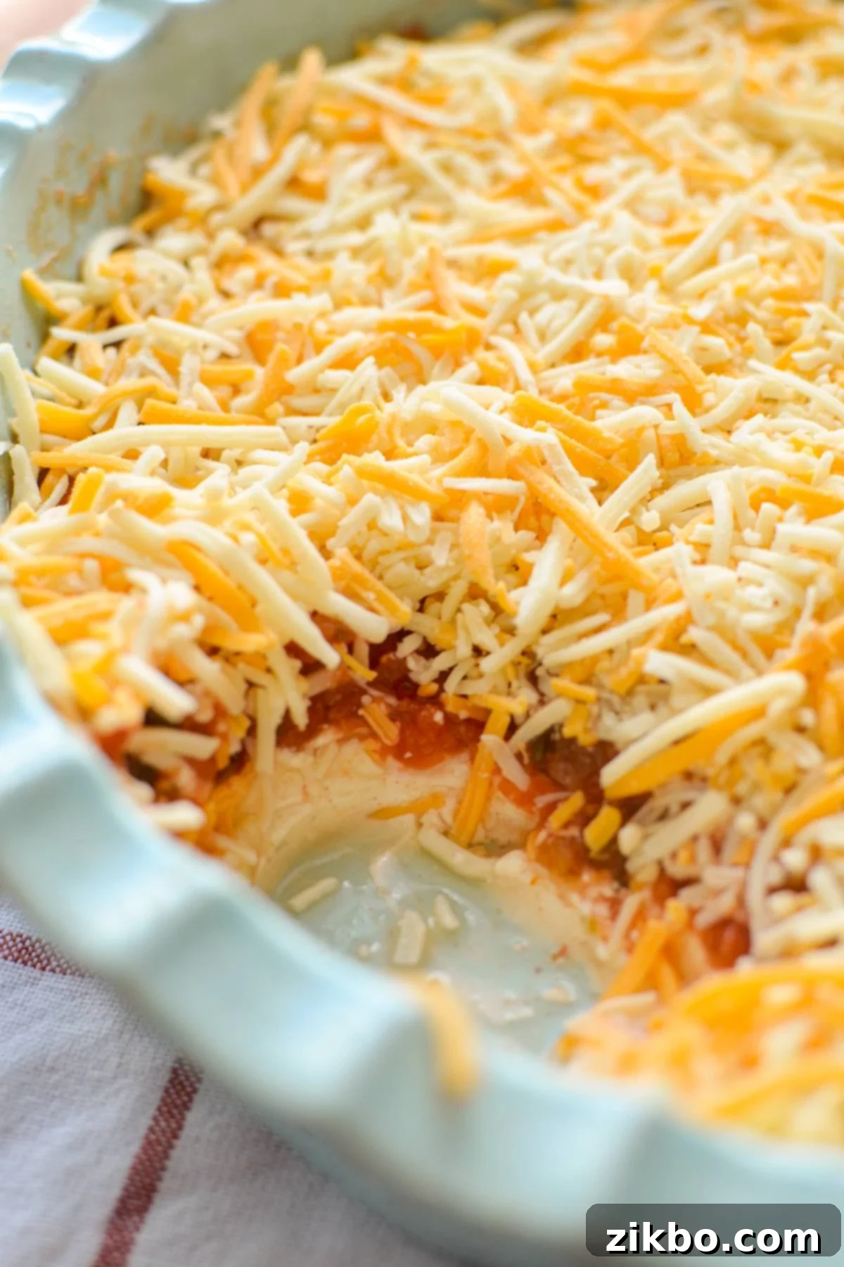 A vibrant, beautifully layered cream cheese and salsa dip, topped with golden shredded cheese, presented in a clear baking dish, ready for serving.
