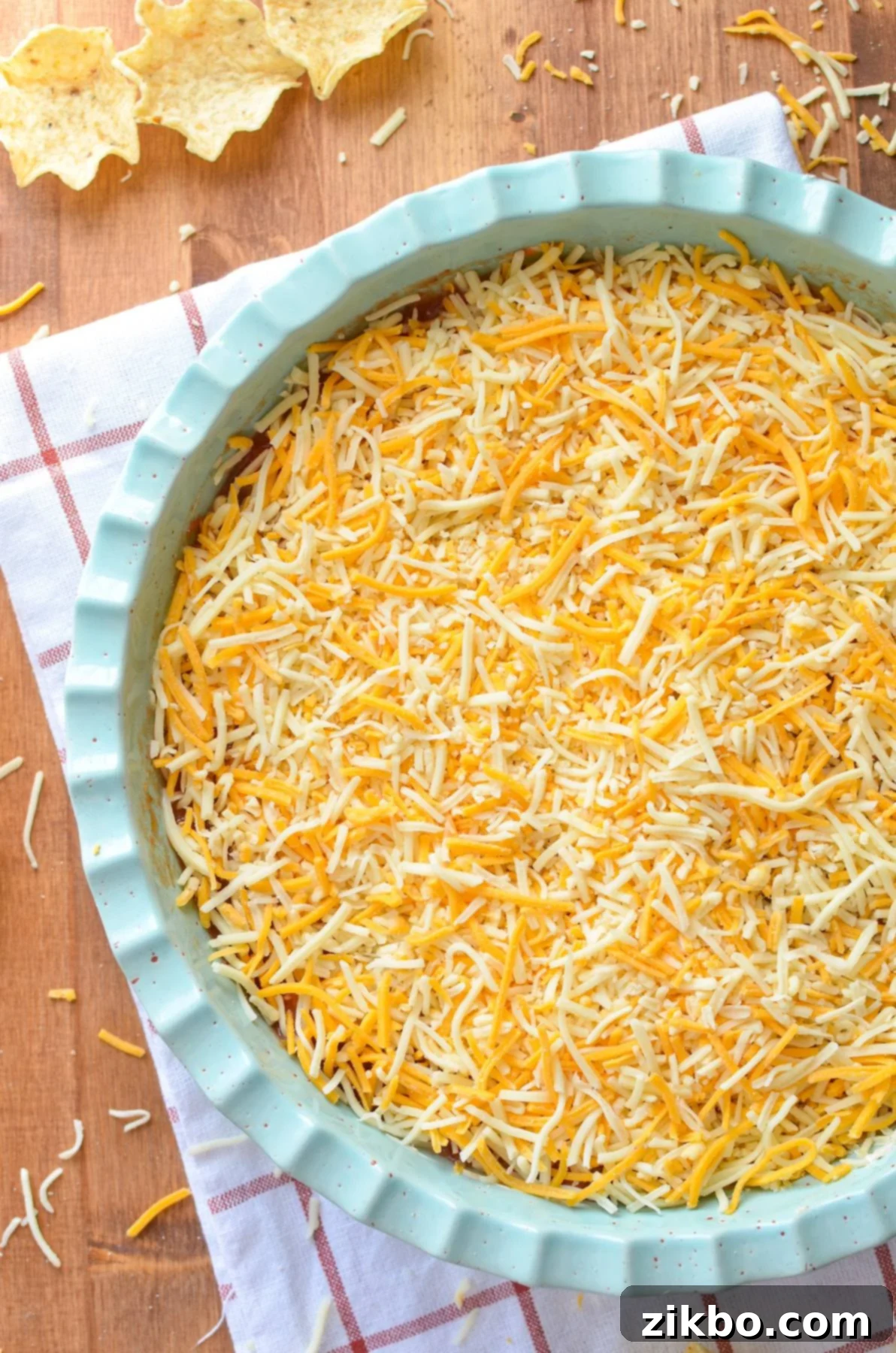 A beautifully layered nacho dip in a round dish, generously topped with golden shredded cheese, perfectly set and ready to be enjoyed with your favorite chips and dippers.
