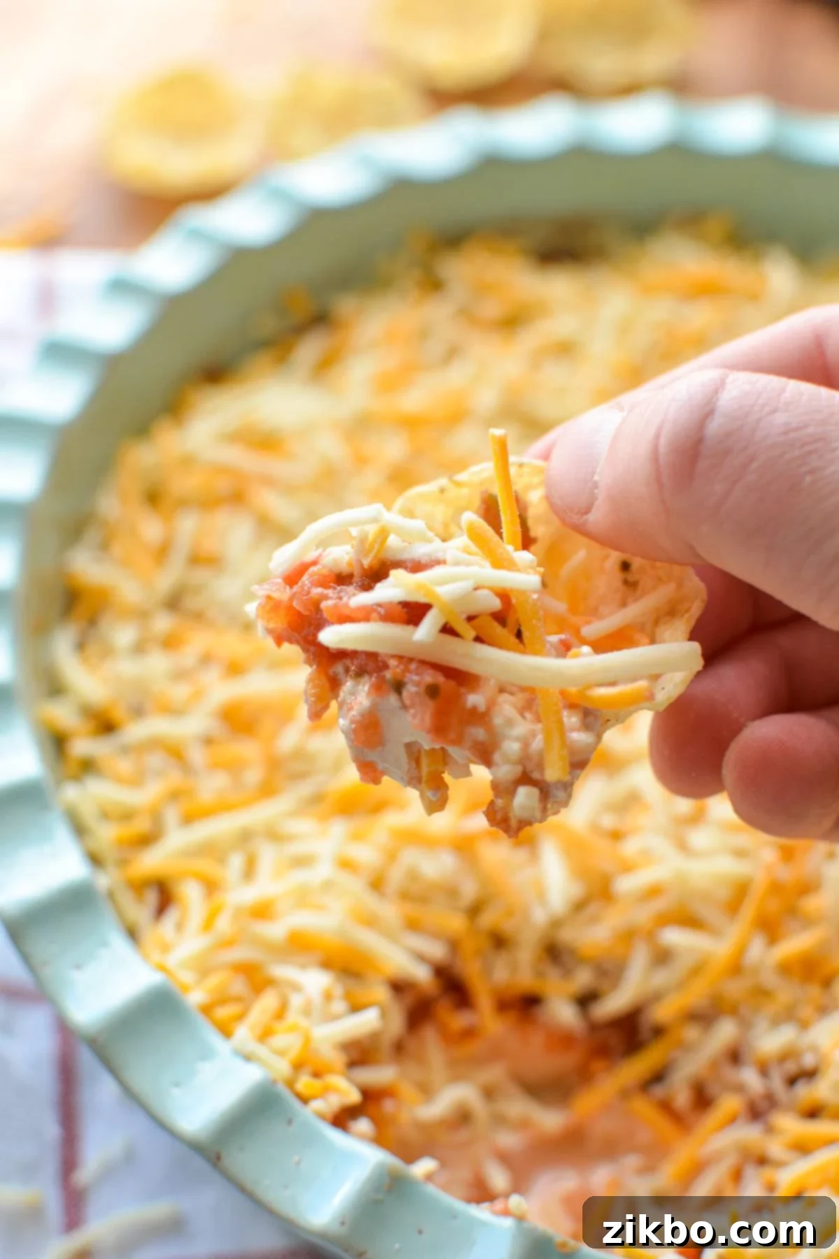A close-up of a tortilla scoop skillfully dipping into a luscious layered cream cheese and salsa dip, capturing the creamy and chunky textures in an inviting shot.