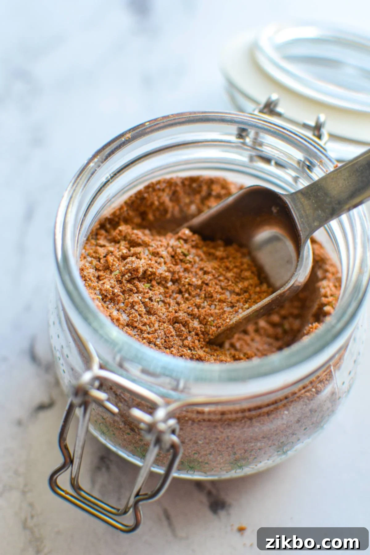 A small jar of homemade taco seasoning with a measuring spoon inside, ready to be used.