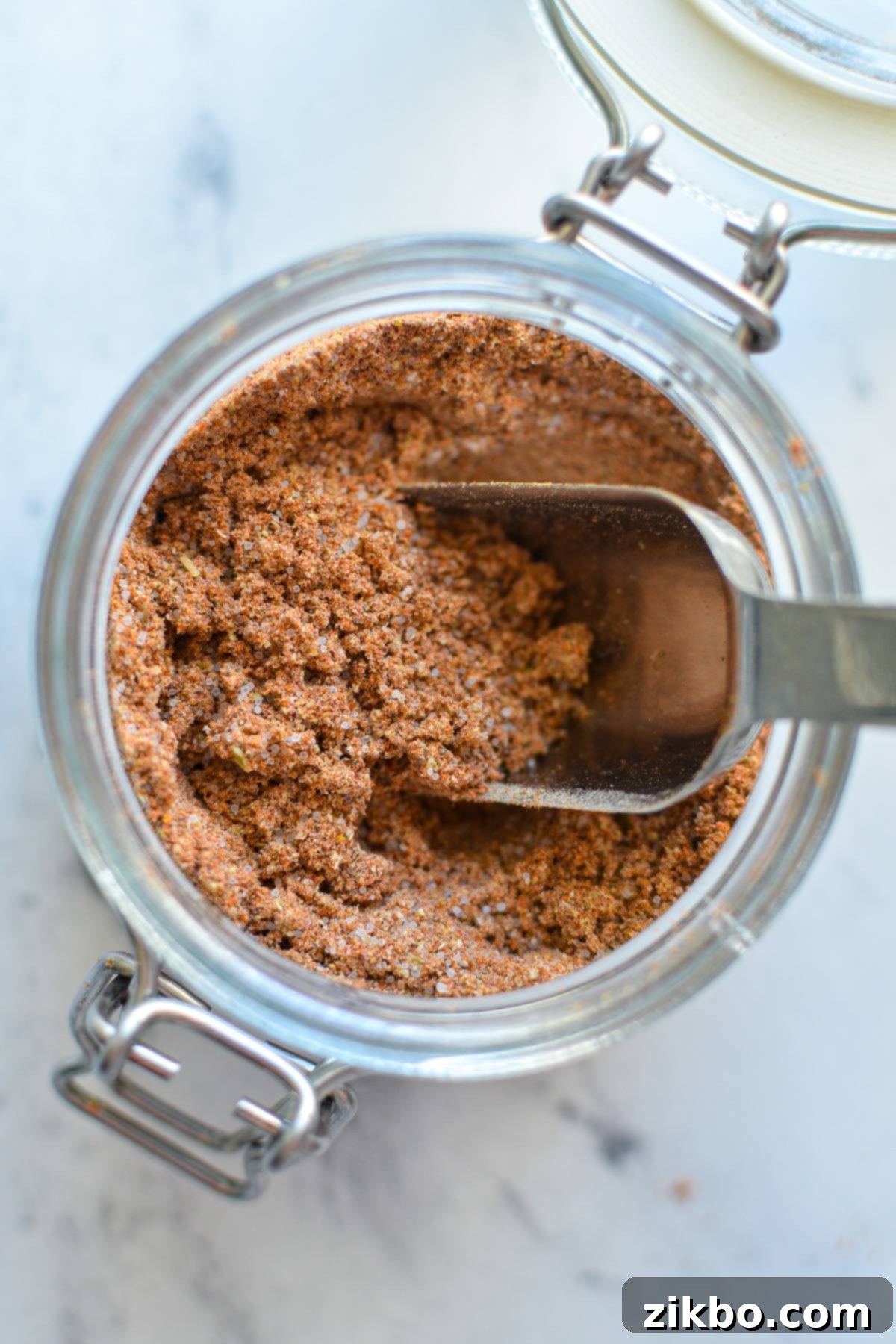 An overhead shot of a jar of homemade taco seasoning with a spoon inside, ready for use.