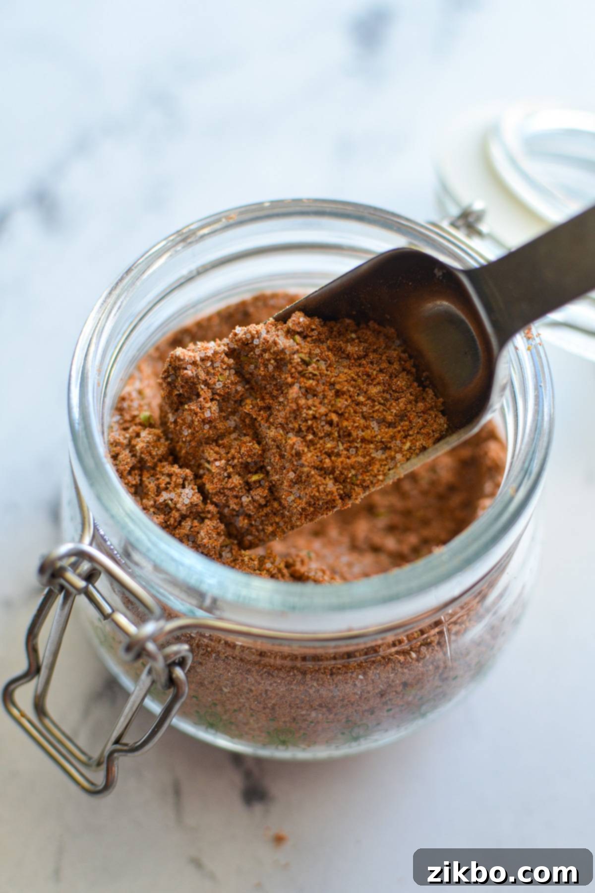 A small jar of homemade taco seasoning with a spoon inside, ready to add flavor to any meal.