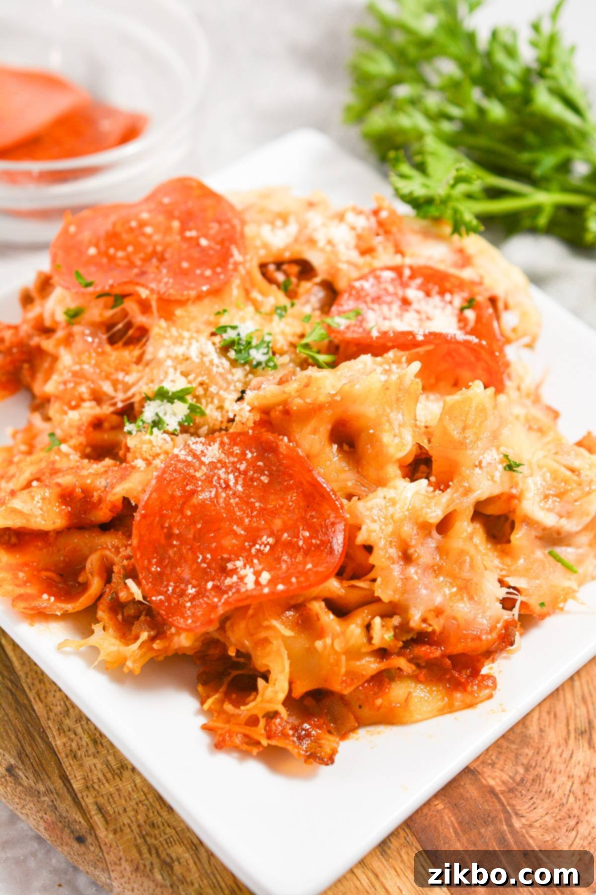 Slow Cooker Pizza Delight 2 A white plate with a generous portion of pizza pasta casserole, garnished with fresh parsley, highlighting the melted cheese and pepperoni.