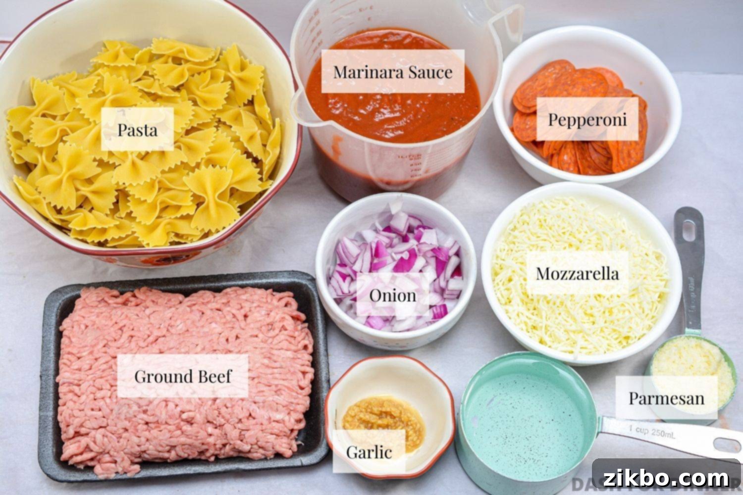Slow Cooker Pizza Delight 3 A flat lay of fresh ingredients laid out on a white surface, including ground beef, a jar of marinara sauce, uncooked bowtie pasta, a pack of pepperoni, shredded mozzarella, and fresh herbs, all ready to make a crock pot pizza casserole.