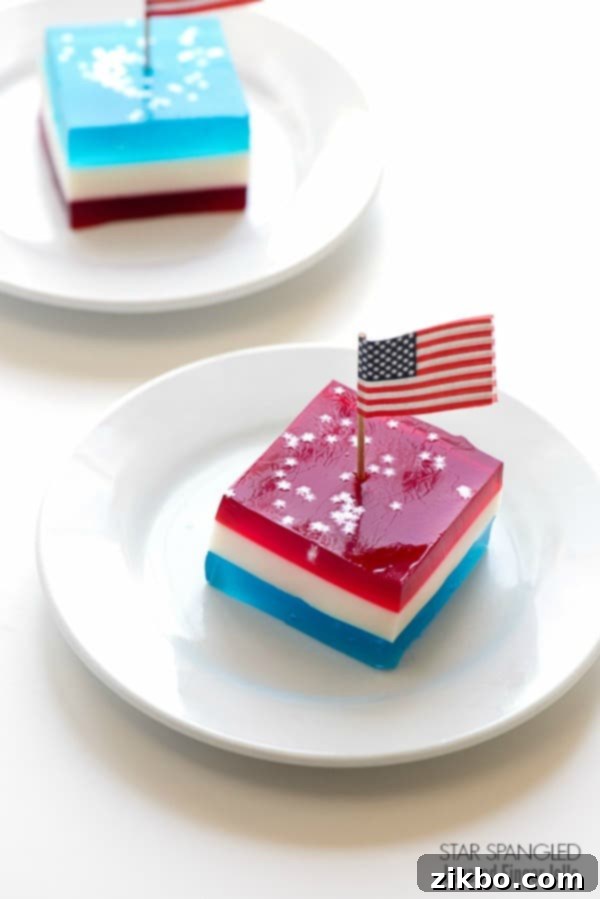 Star Spangled Layered Finger Jello, a creamy red, white, and blue dessert, garnished with mini American flags for patriotic appeal.