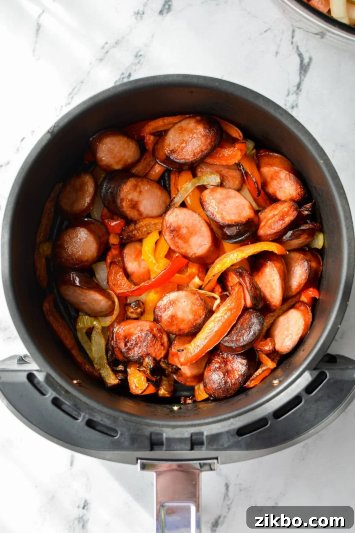 An overhead shot of an air fryer with cooked sausage and peppers.