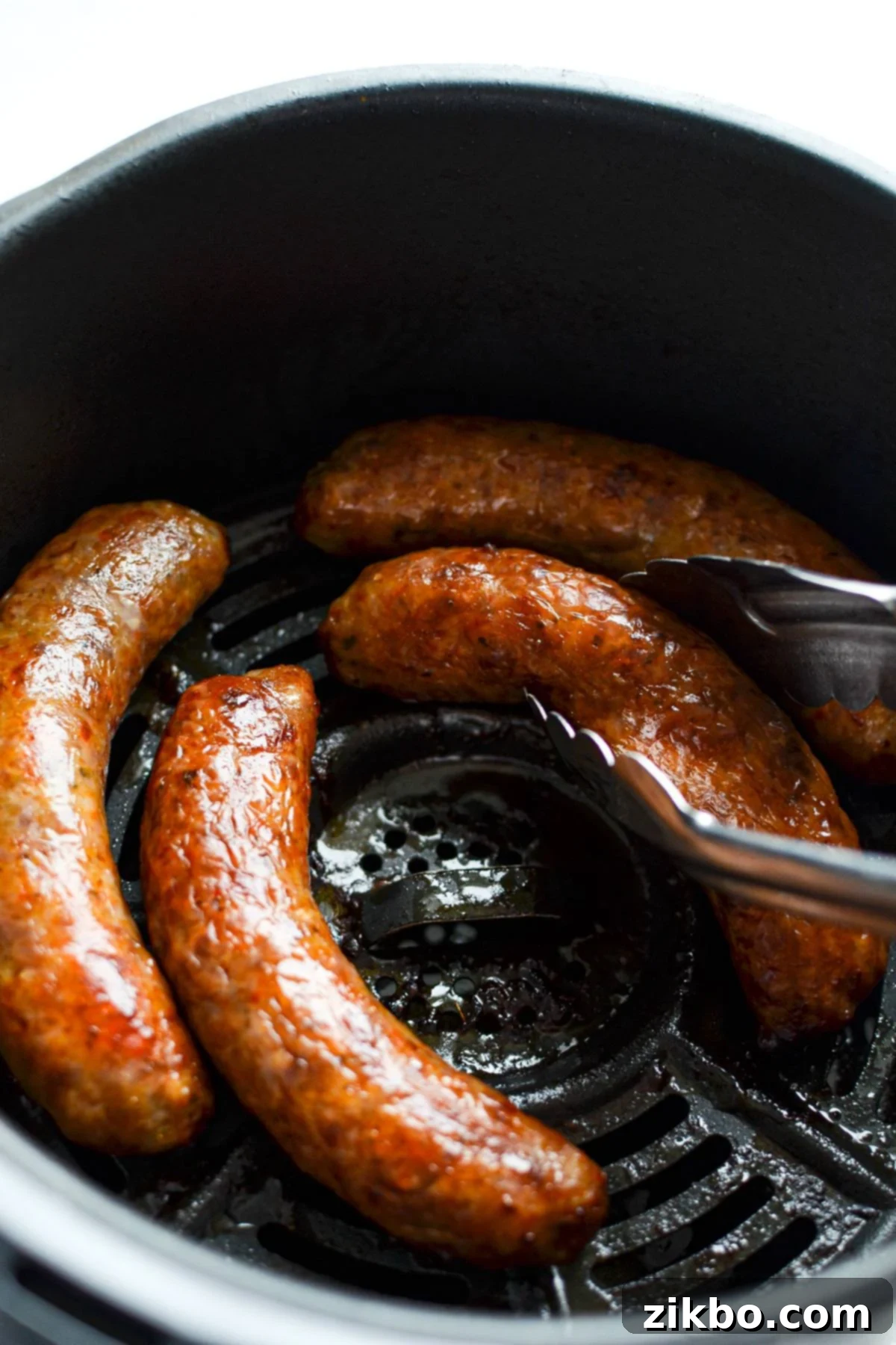 Tongs pulling Italian sausages out of an air fryer.