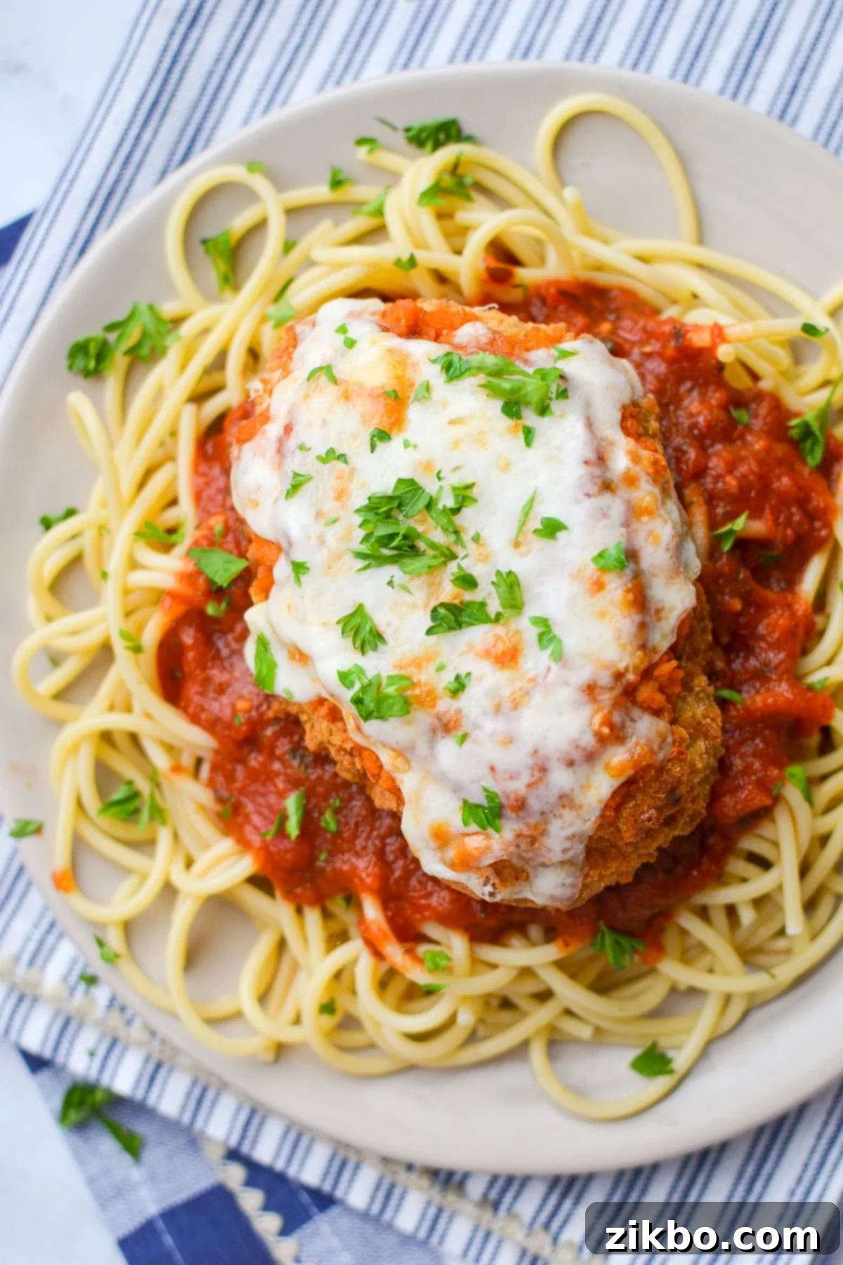 A plate of spaghetti noodles with chicken parmesan and marinara sauce.