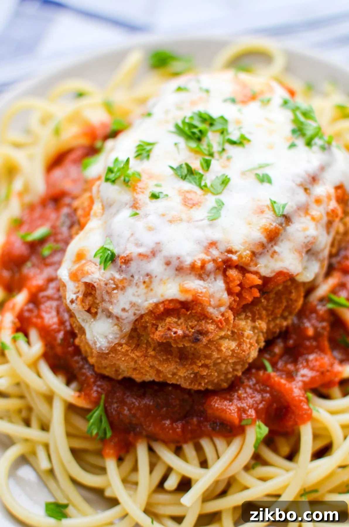 A cutlet of air fryer frozen chicken parmesan on top of a bed of cooked spaghetti.