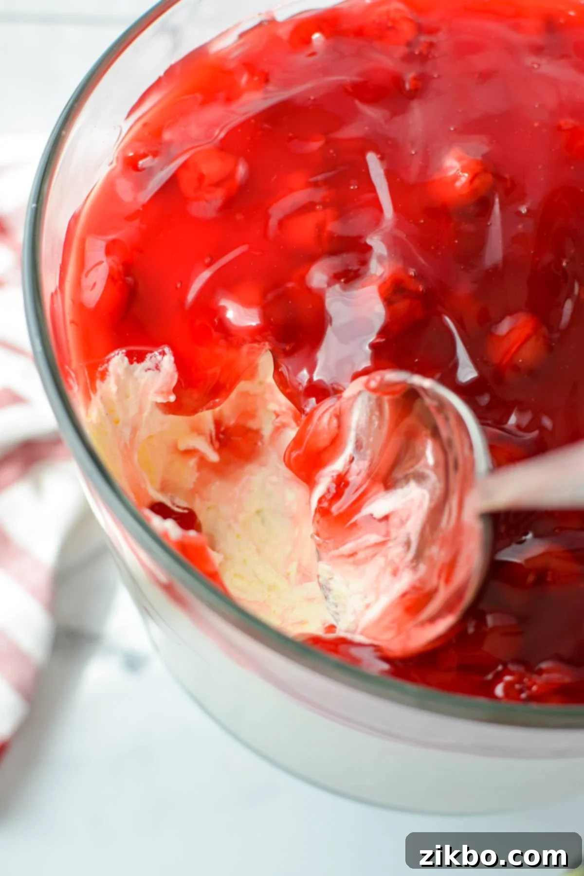 A spoon scooping out a generous portion of lazy cheesecake salad, revealing its creamy texture and fruity topping.