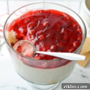 A trifle dish filled with no bake cheesecake and a cherry pie filling.
