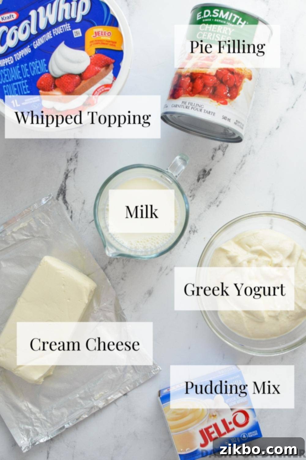 The six simple ingredients laid out for making a quick no-bake cheesecake salad: cream cheese, whipped topping, yogurt, pudding mix, milk, and pie filling.
