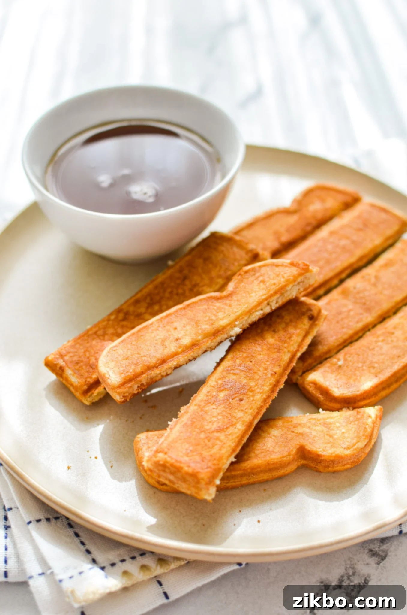 A plate of golden-brown air fryer frozen french toast sticks with a small bowl of rich maple syrup on the side, ready for dipping.