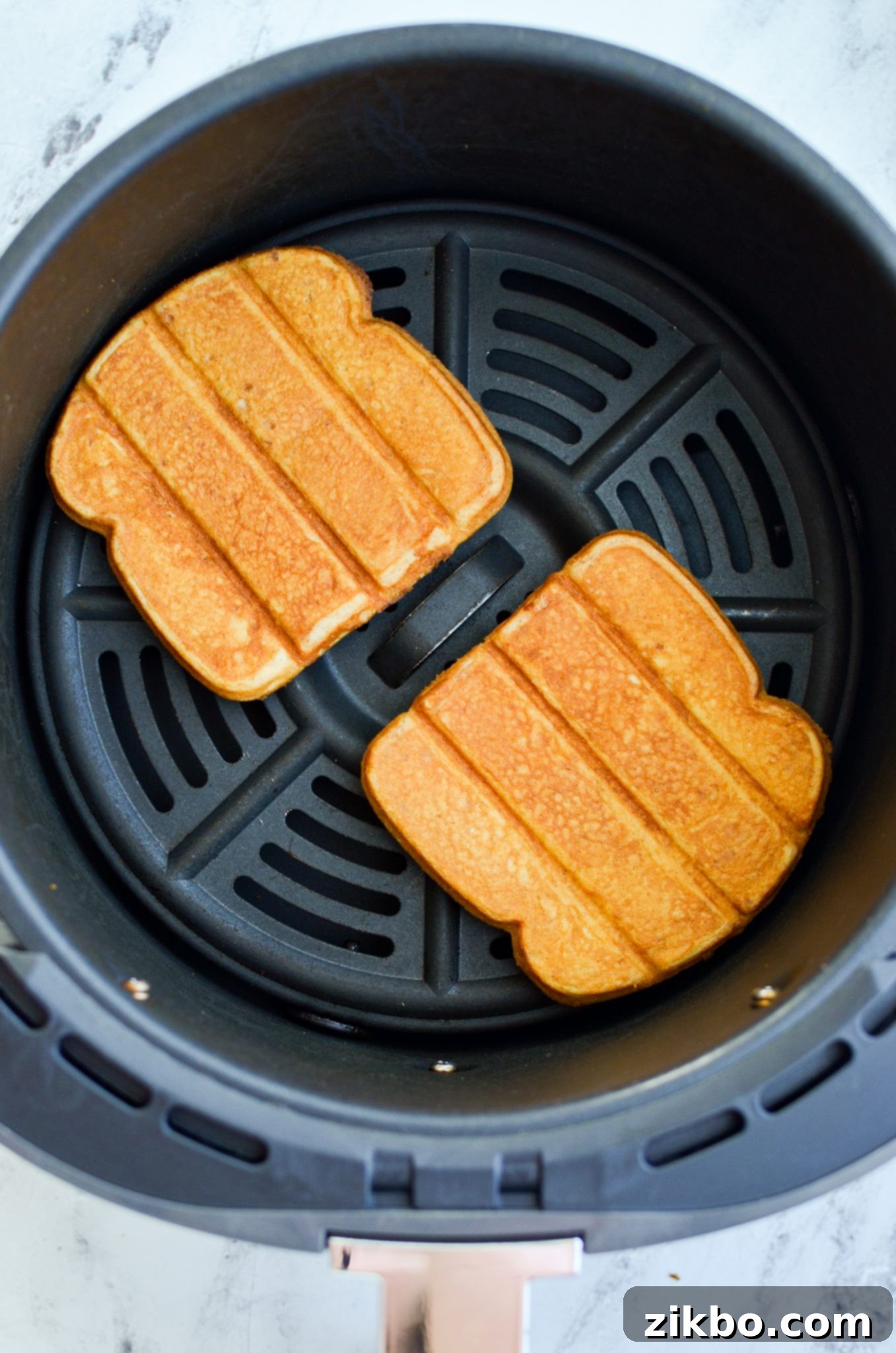 Frozen French toast sticks being placed into an air fryer basket in a single layer.
