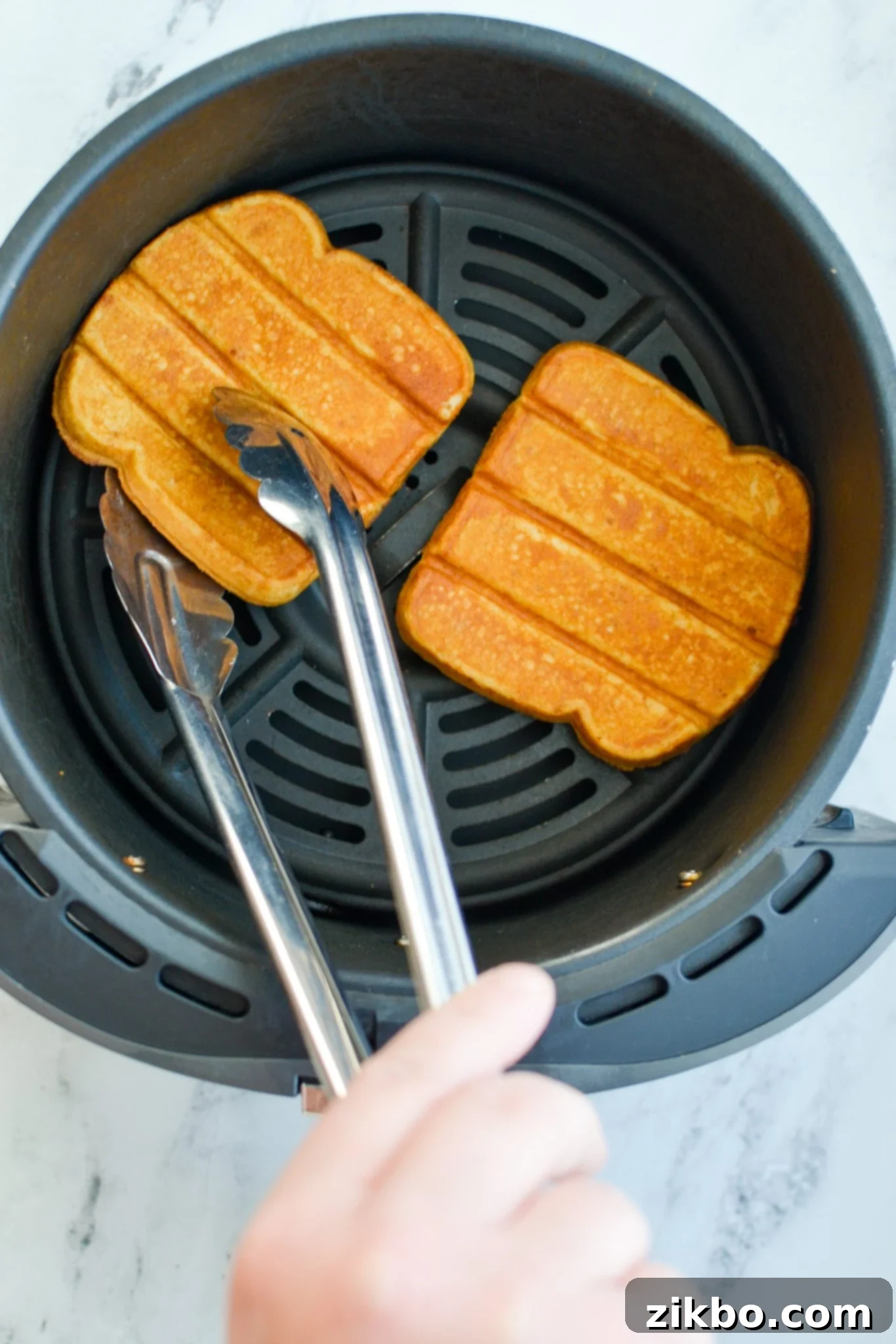 Hand flipping frozen French toast sticks over in the air fryer basket halfway through cooking.