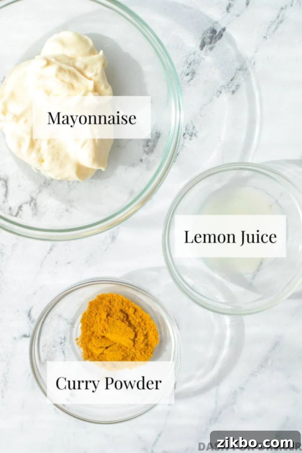 Three small bowls neatly arranged on a counter, containing creamy mayonnaise, bright yellow curry powder, and freshly squeezed lemon juice – the simple ingredients for homemade curry mayo.