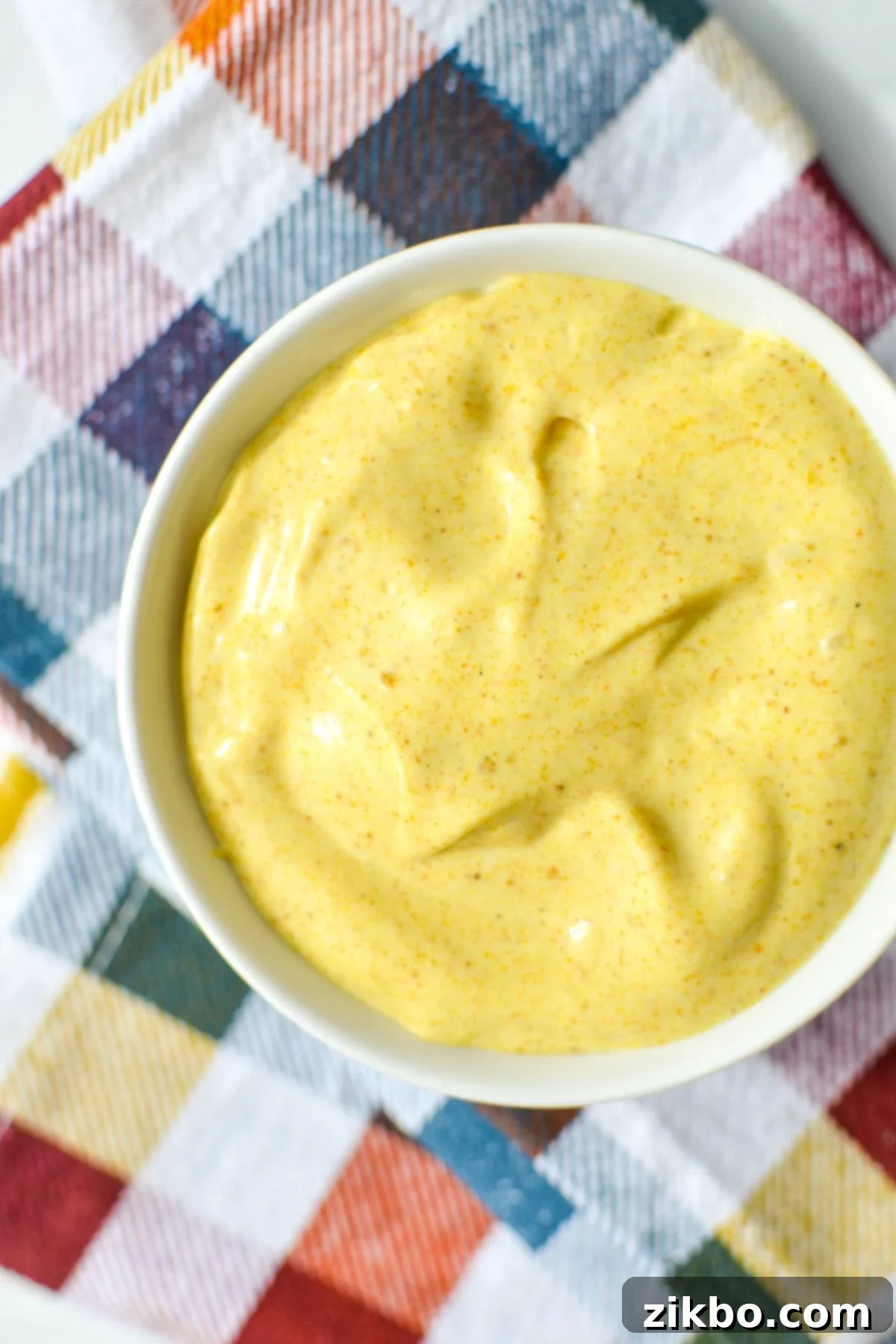 A small bowl of golden homemade curry aioli, elegantly placed on a charming checked napkin, ready for dipping.
