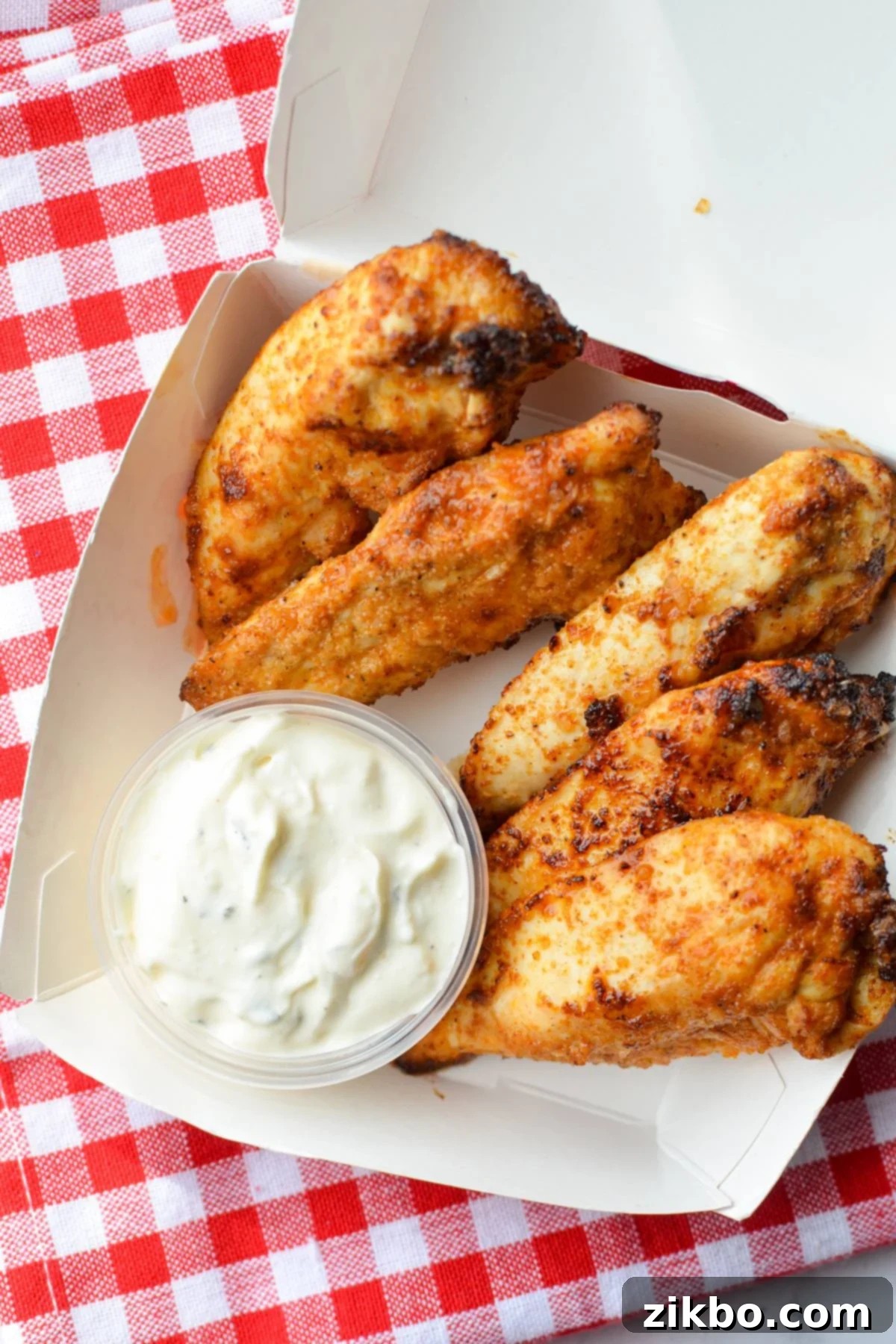 A small takeout box with homemade unbreaded chicken tenders and ranch dip.