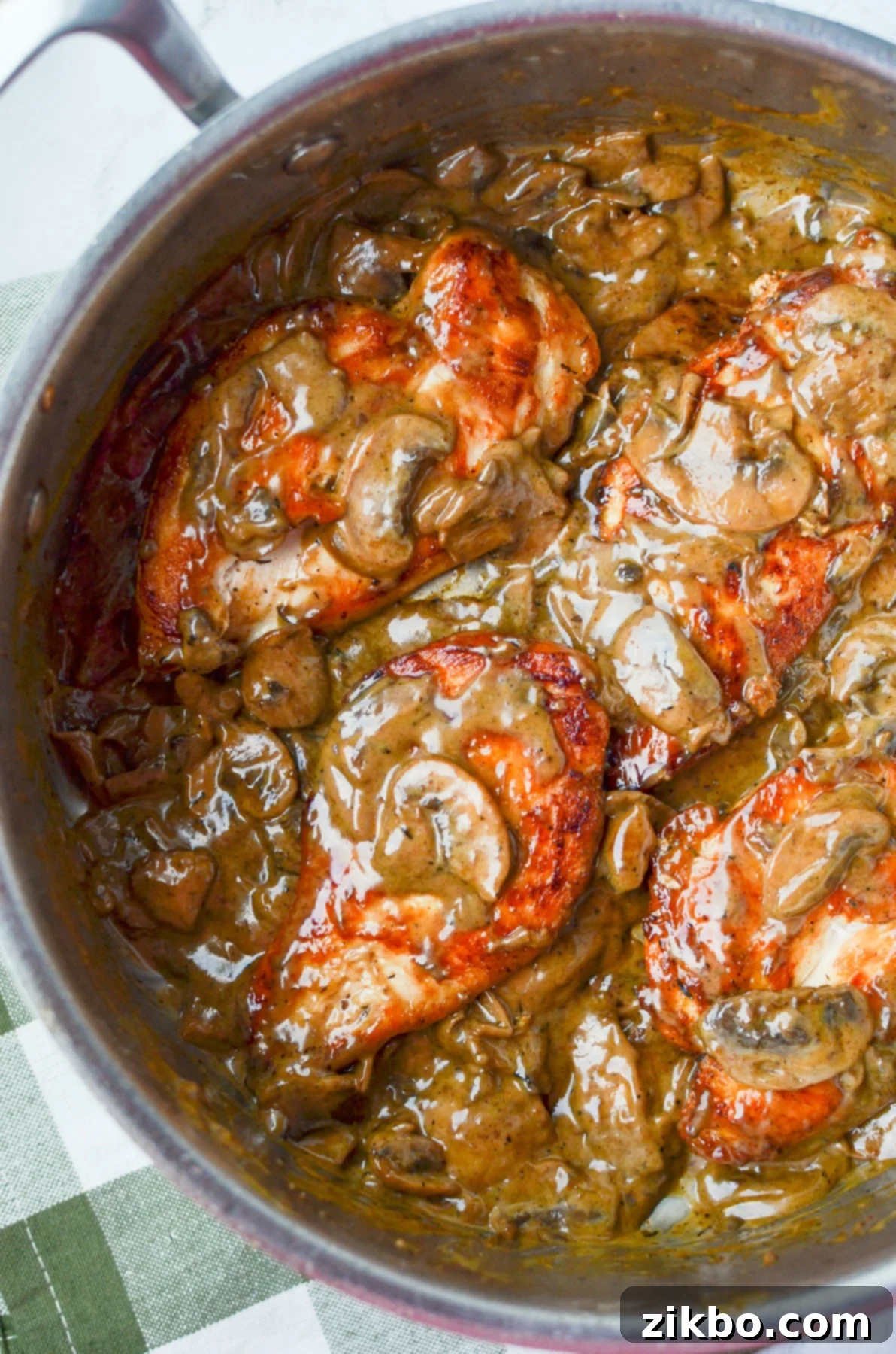 A skillet filled with chicken breasts covered in a creamy mushroom sauce.