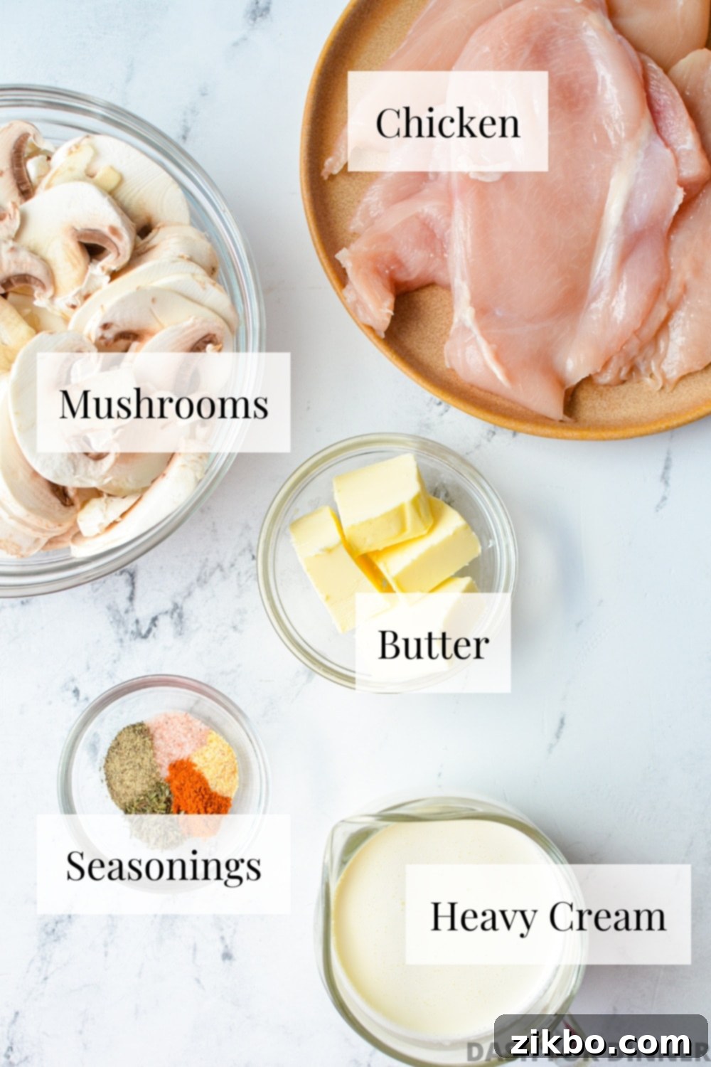 Chicken breasts, mushrooms, butter, seasonings, and heavy cream on a marble background.