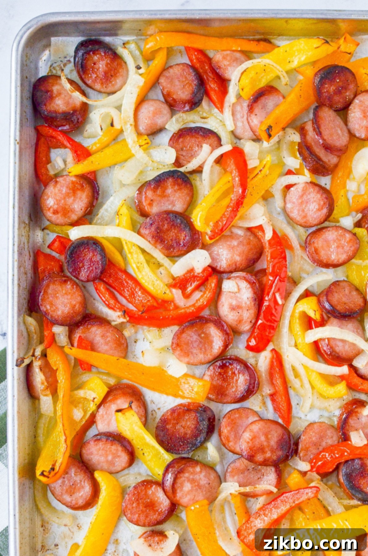 A sheet pan filled with sliced sausages, bell peppers, and onions, perfectly roasted.