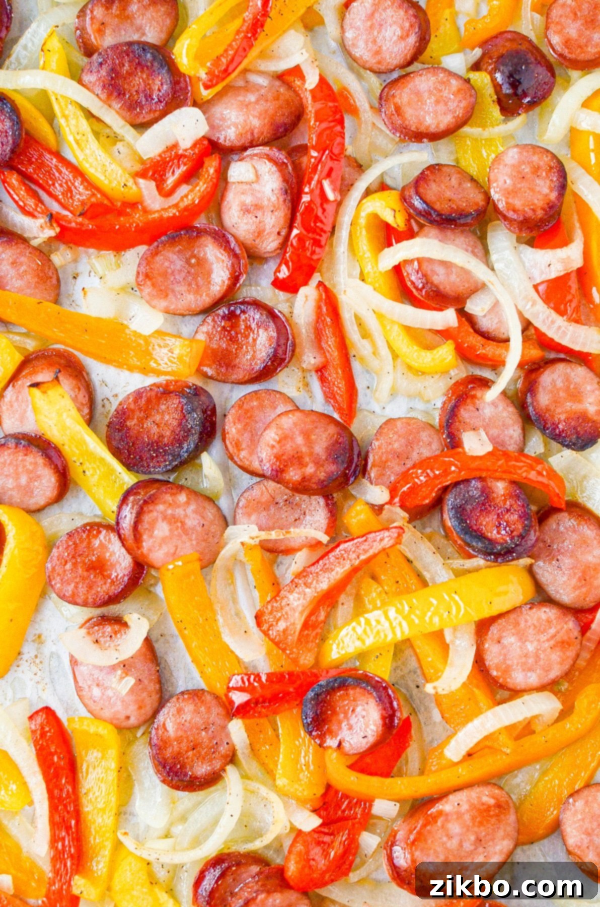 Sausage rounds, peppers, and onions spread on a sheet pan, cooked to perfection.